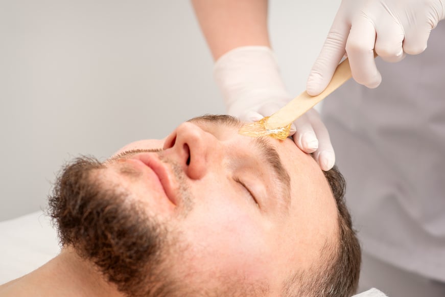 Beautician Applying Wax Paste between Eyebrows during the Procedure of Waxing in the Beauty Salon.